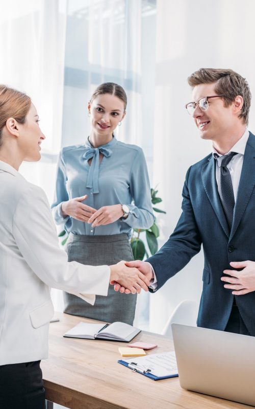 cheerful-recruiter-shaking-hands-with-woman-near-colleague-in-office.jpg